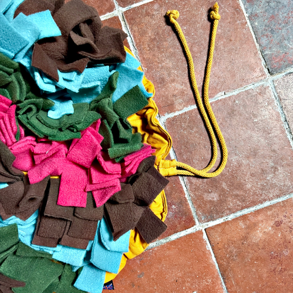 ON A TILED FLOOR, A YELLOW STYLISH DOG TOY USED FOR A SNUFFLE MAT FOR DOG BEHAVIOUR SEPARATION ANXIETY FOR DOGS , DESIGNED BY LISH LONDON  